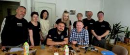 Grupa ludzi uśmiecha się do zdjęcia przed stołem, na którym widać słodki poczęstunek i dron