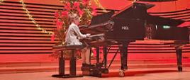 Dziewczynka gra na fortepianie, za którym stoi udekorowana choinka.