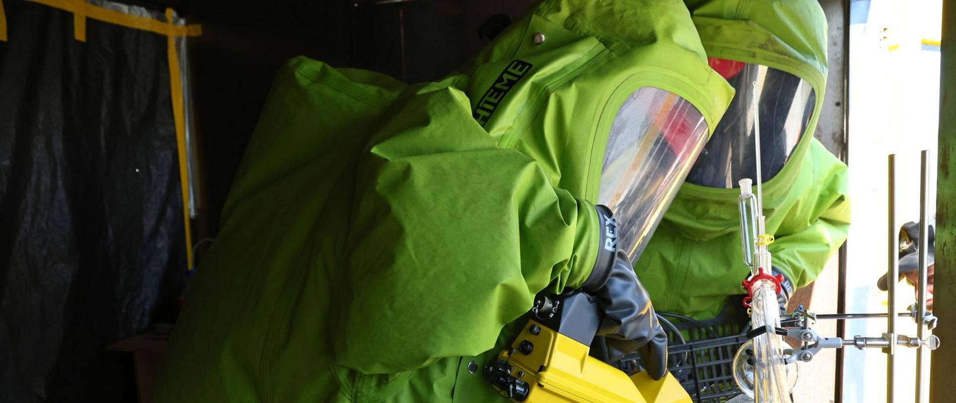 Dwóch uczestników specjalistycznego szkolenia w zakresie przeciwdziałania zagrożeniom chemicznym, biologicznym, radiologicznym, nuklearnym i wybuchowym ubranych w kombinezon gazoszczelny podczas ćwiczeń