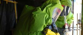 Dwóch uczestników specjalistycznego szkolenia w zakresie przeciwdziałania zagrożeniom chemicznym, biologicznym, radiologicznym, nuklearnym i wybuchowym ubranych w kombinezon gazoszczelny podczas ćwiczeń