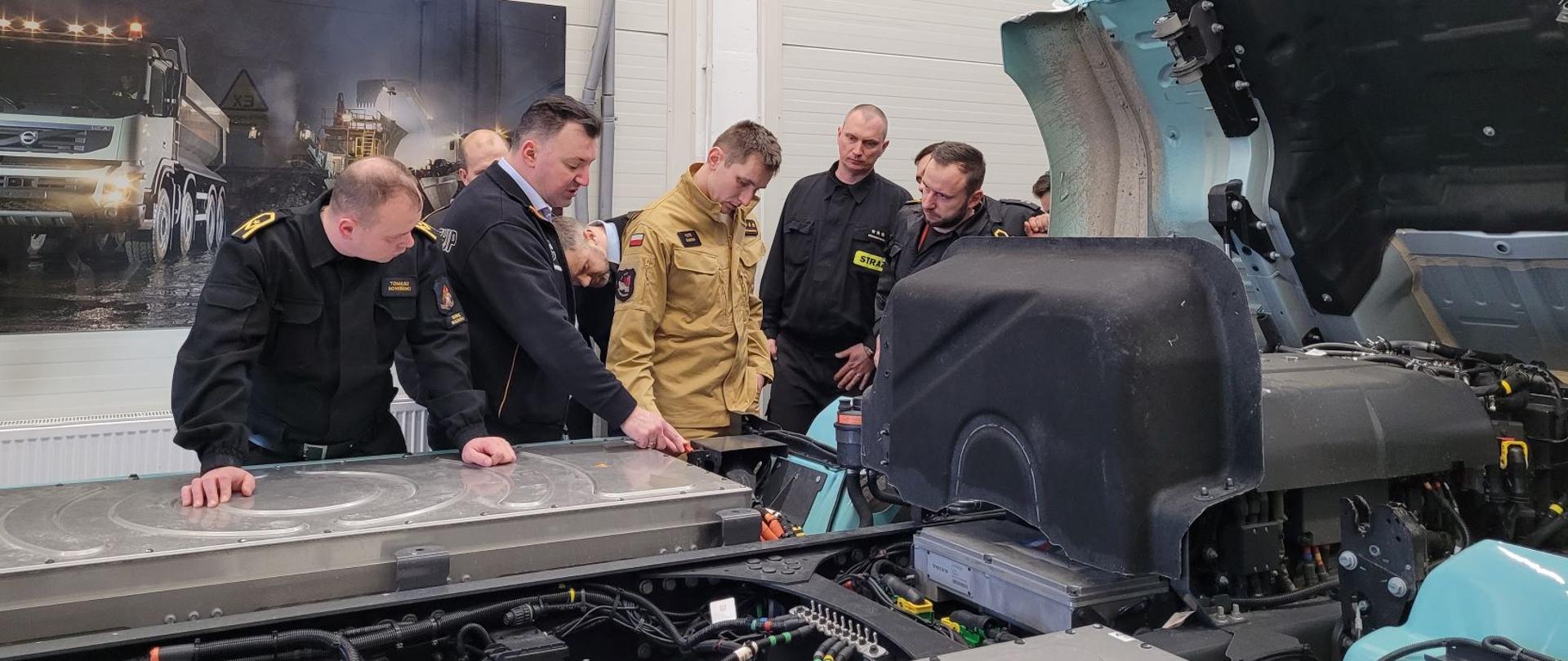 Strażacy stojący przy samochodzie razem z przedstawicielem firmy 