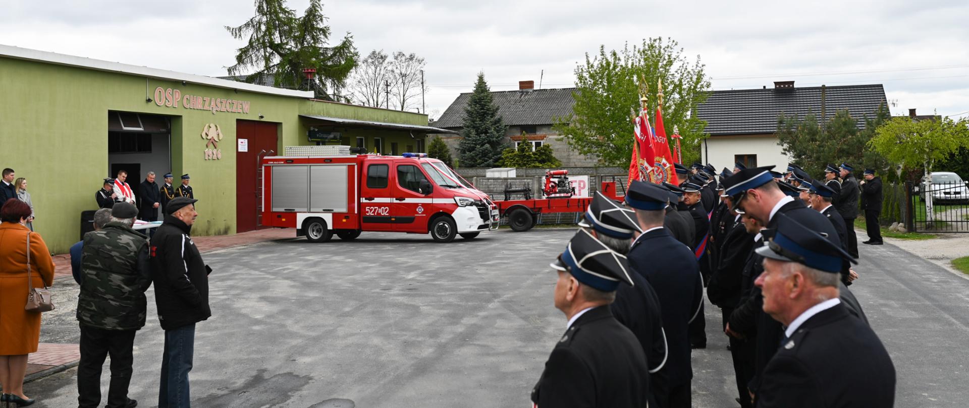 po lewej budek remizy OSP Chrząszczew przed nim samochód pożarniczy po prawej druhowie i poczty sztandarowe