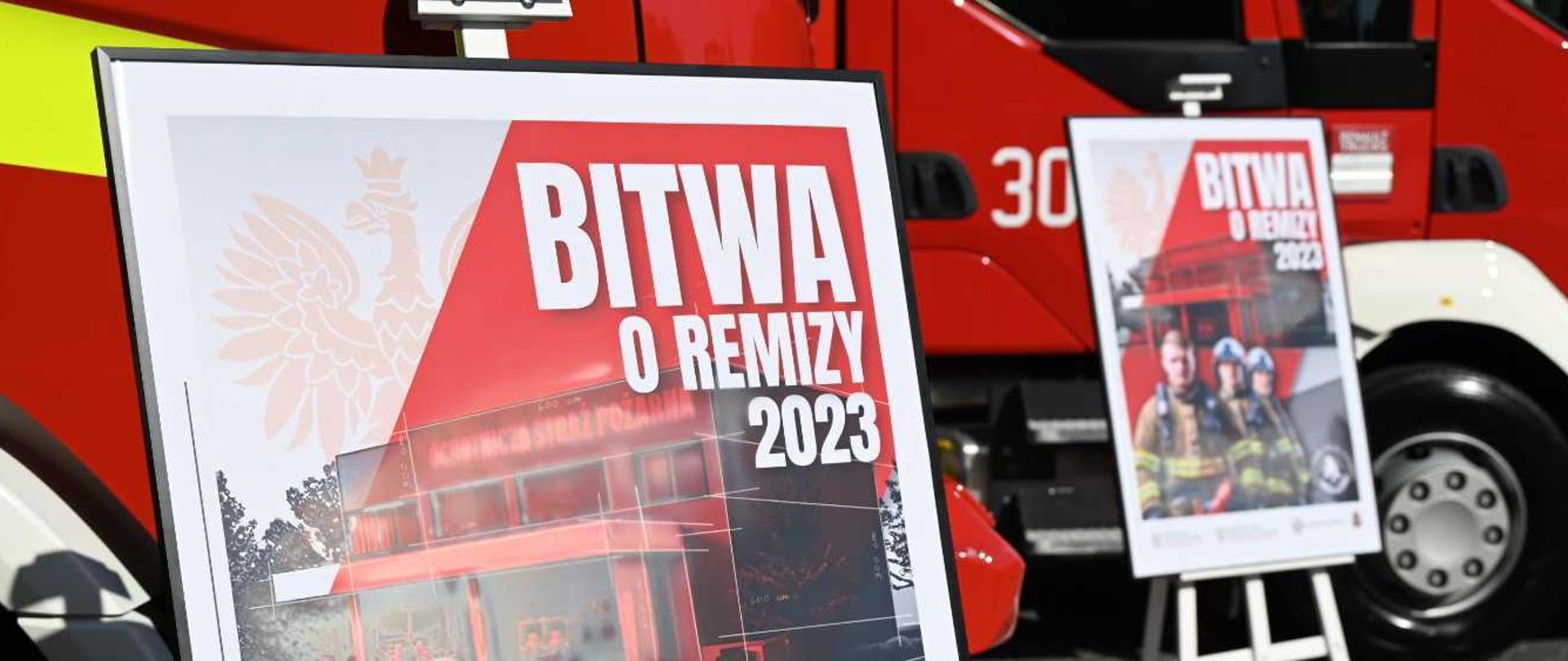  Dwa plakaty promocyjne akcji „Bitwa o Remizy 2023” na tle dwóch pojazdów pożarniczych.