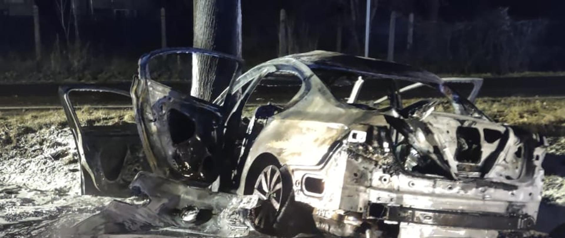 Zdjęcie wykonane w porze nocnej. Widać wrak auta osobowego. Zdjęcie wykonane na drodze publicznej. Oświetlenie sztuczne.