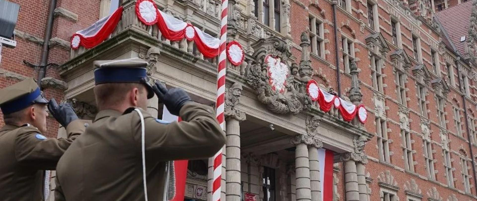 Żołnierze wojska polskiego oddający honory podczas uroczystości podniesienia flagi państwowej, w tle urząd wojewódzki.