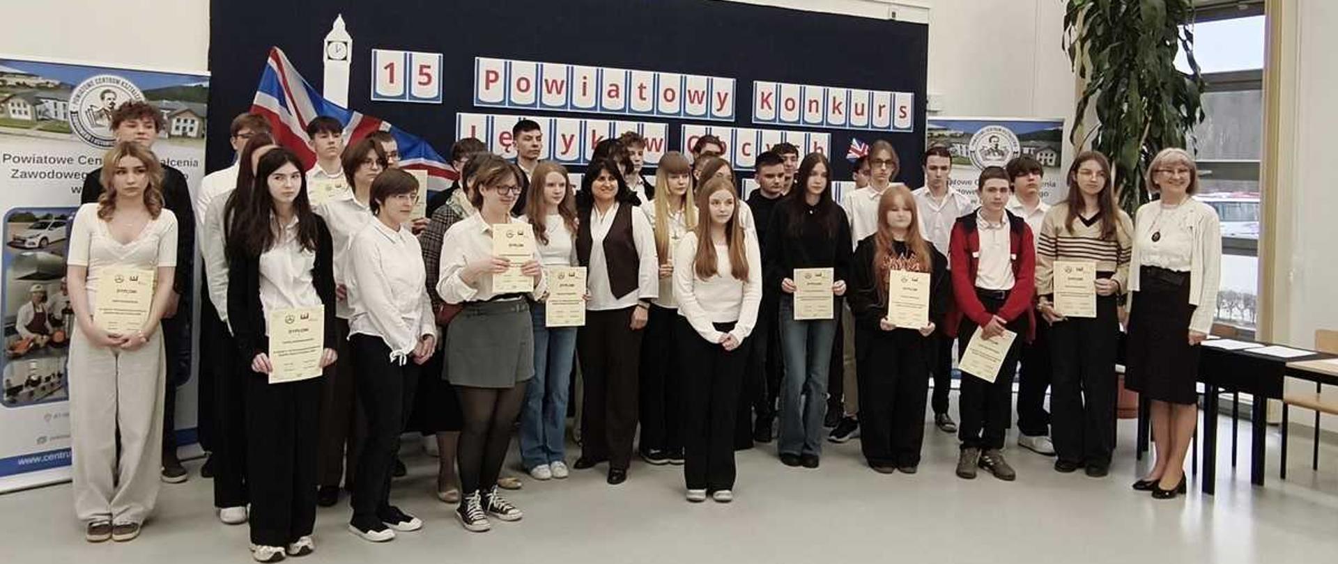 Zdjęcie przedstawia grupę osób, prawdopodobnie uczniów oraz nauczycieli, podczas uroczystego podsumowania 15. Powiatowego Konkursu w Centrum Kształcenia Zawodowego i Ustawicznego.
Na zdjęciu widoczni są uczestnicy konkursu trzymający dyplomy oraz osoby dorosłe, które prawdopodobnie są organizatorami lub nauczycielami.
W tle znajduje się napis wskazujący na placówkę oświatową: „Centrum Kształcenia Zawodowego i Ustawicznego”.
Dekoracja ściany potwierdza wydarzenie: „15. Powiatowy Konkurs”.
Całość ukazuje oficjalne wydarzenie edukacyjne o charakterze powiatowym, odbywające się w szkole.