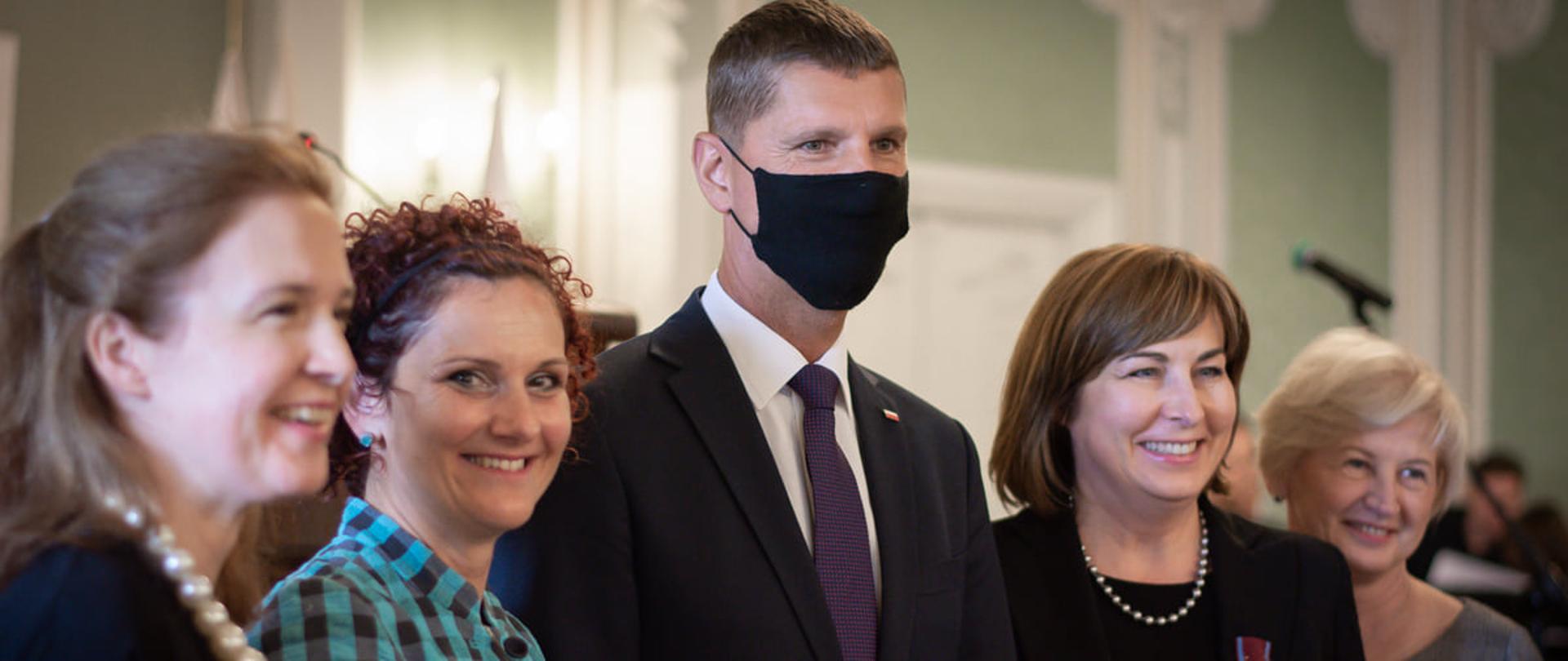 Dzień Edukacji Narodowej w Białymstoku z udziałem wiceministra Dariusza Piontkowskiego, wiceminister Dariusz Piontkowski stoi w towarzystwie odznaczonych nauczycielek, ma na sobie maseczkę.