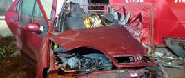 Czerwony samochód osobowy marki Renault stoi na chodniku cały zgnieciony po wypadku
