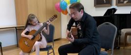 Na krzesłach zasiadają na środku sali gitarzyści - młoda dziewczynka i jej nauczyciel.