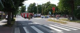 Zdjęcie przedstawia kolizję z udziałem 3 samochodów osobowych. Na zdjęciu widać pojazdy ratowniczo - gaśnicze oraz strażaków biorących udział w działaniach. Na dalszym planie widoczny radiowóz policji oraz karetka pogotowia ratunkowego Zdjęcie wykonane w porze dziennej na ulicy.