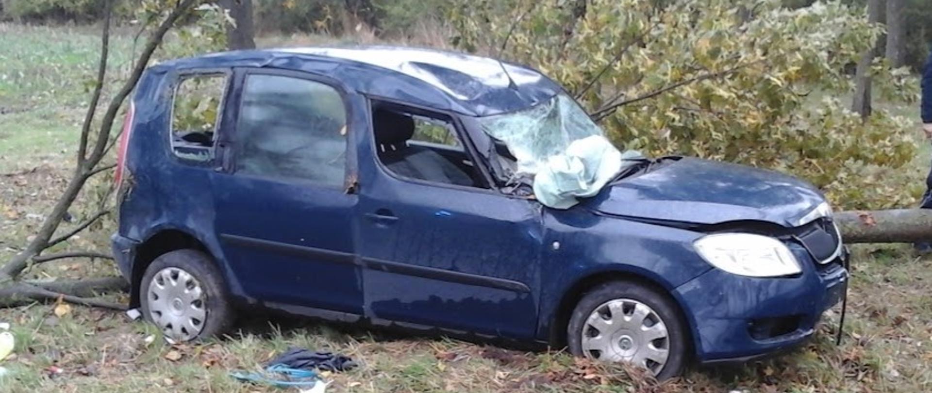 Rozbity samochód osobowy marki Skoda stojący na poboczu jezdni po uderzeniu w drzewo. 