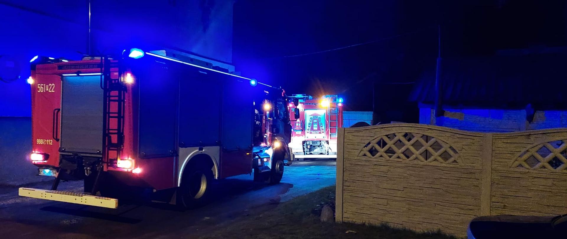 Noc dwa oświetlone niebieskimi sygnałami świetlnymi auta strażay pożarnej stoją w rzędzie przy budynku mieszkalnym
