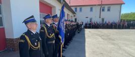 Zdjęcie przedstawia teren Jednostki Ratowniczo-Gaśniczej oraz strażaków ubranych w mundury galowe koloru czarnego ze sznurem galowym oraz czapką rogatywką na głowie, podczas obchodów Dnia Strażaka w Radziejowie. Na zdjęciu ustawiony w szeregu pododdział strażaków Komendy Powiatowej Państwowej Straży Pożarnej wraz z dowódcą oraz sztandarem. 