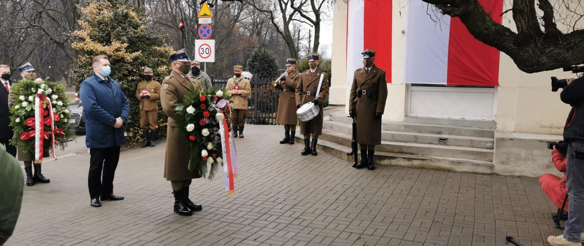 Żołnierze Wojska Polskiego ubrani w mundury. Jeden z nich gra na bębnie, inny na trąbce. Po środku jeden żołnierz z wieńcem. Tuż za nim minister Przemysław Czarnek. Dookoła żołnierze ze zniczami w rękach. 