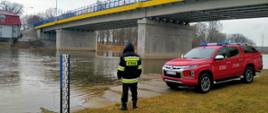 Zdjęcie przedstawia most na rzece Warta w Skwierzynie. Strażak obserwuje poziom rzeki. Pojazd operacyjny.