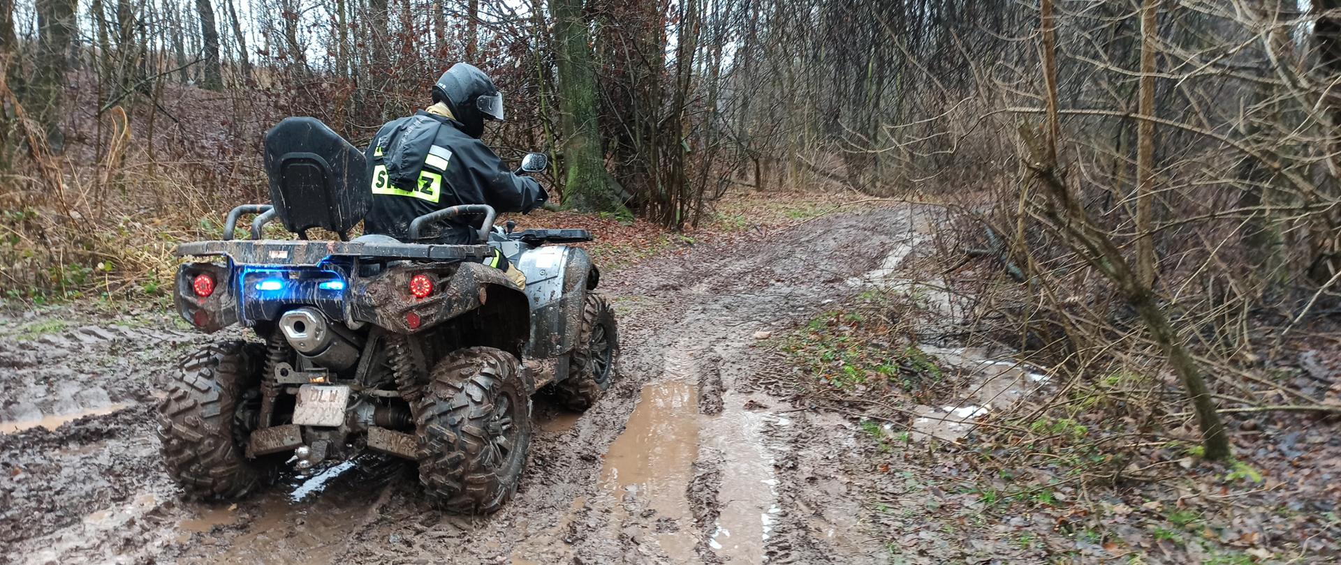 Zdjęcie przedstawia strażaka poruszającego się pojazdem terenowym drogą leśną po grząskim terenie. 