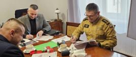 Przedstawiciele Państwowej Straży Pożarnej i partnerów instytucjonalnych podpisują dokumenty podczas spotkania roboczego w gabinecie.
