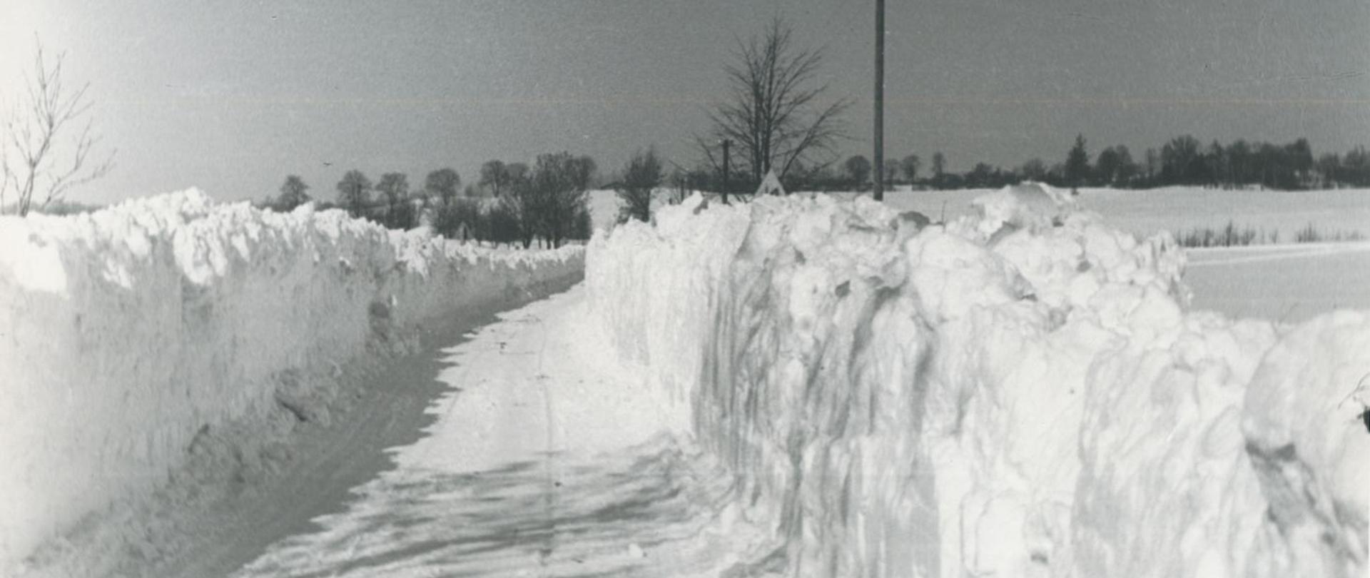 Zima, droga wśród zasp, w tle drzewa i pola, zdjęcie czarno-białe