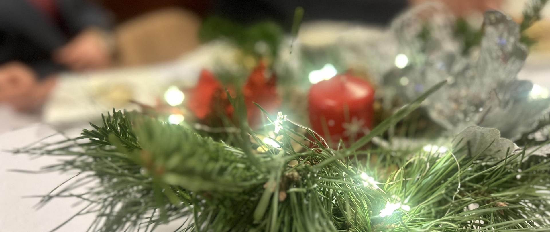 stroik bożonarodzeniowy z czerwoną świecą stojący na stole z białym obrusem