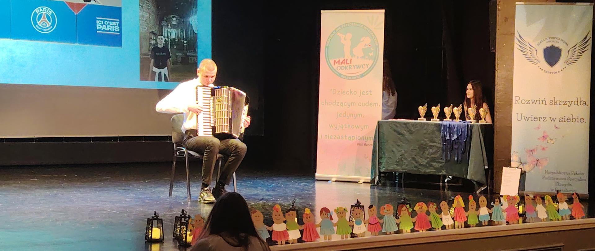 Zdjęcie przedstawiające na scenie Teatru Starego w Bolesławcu - Necmiego Demira, który siedzi na krześle z akordeonem. Necmi wystąpił w ramach obchodów Światowego Dnia Świadomości o Autyzmie - IV Gali Talentów, która odbyła się 22 kwietnia 2026 roku.