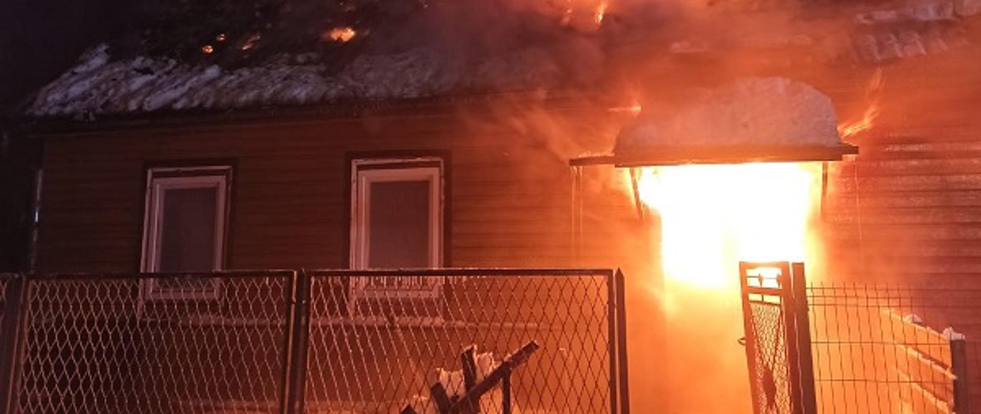 Zdjęcie przedstawia pożar budynku mieszkalnego w miejscowości Supraśl. Płomieniami objęte jest całe poddasze oraz okolice klatki schodowej na parterze.