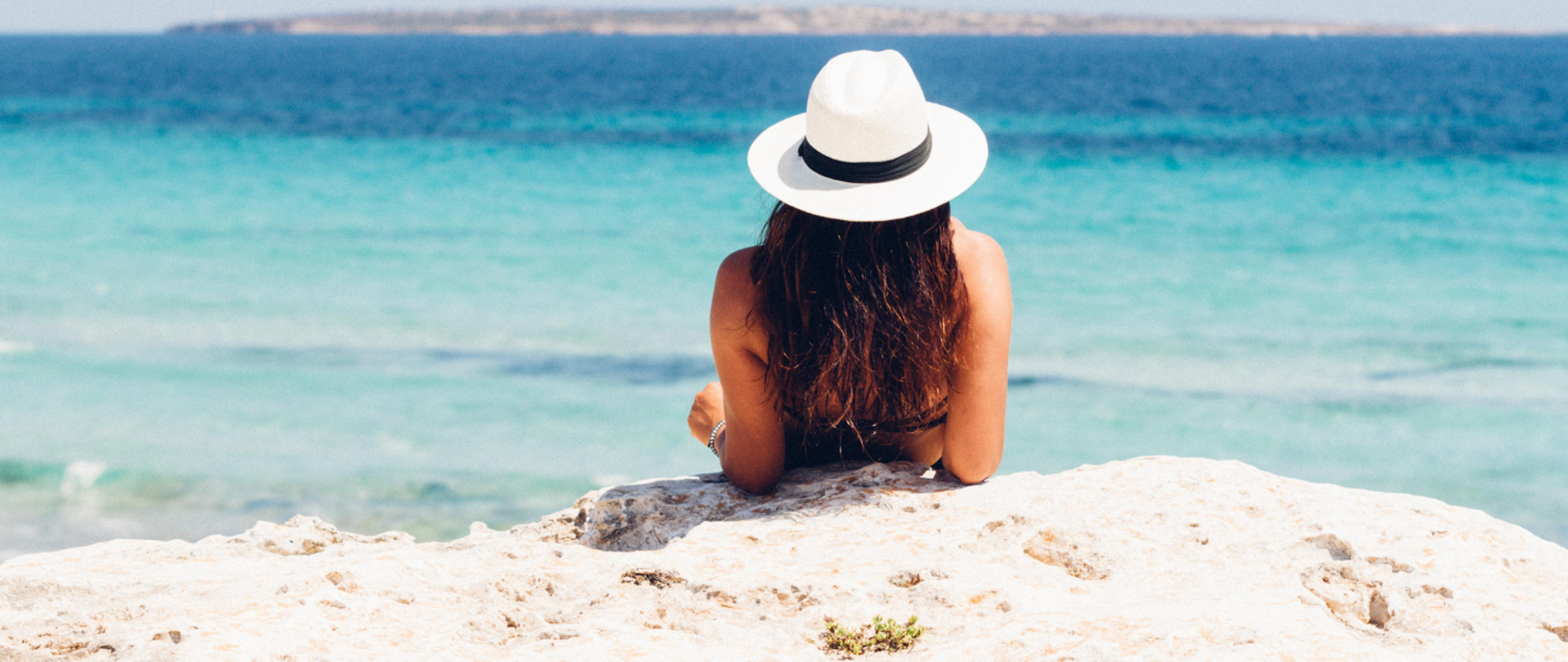 kobieta w kapeluszu opala się na skalistej plaży