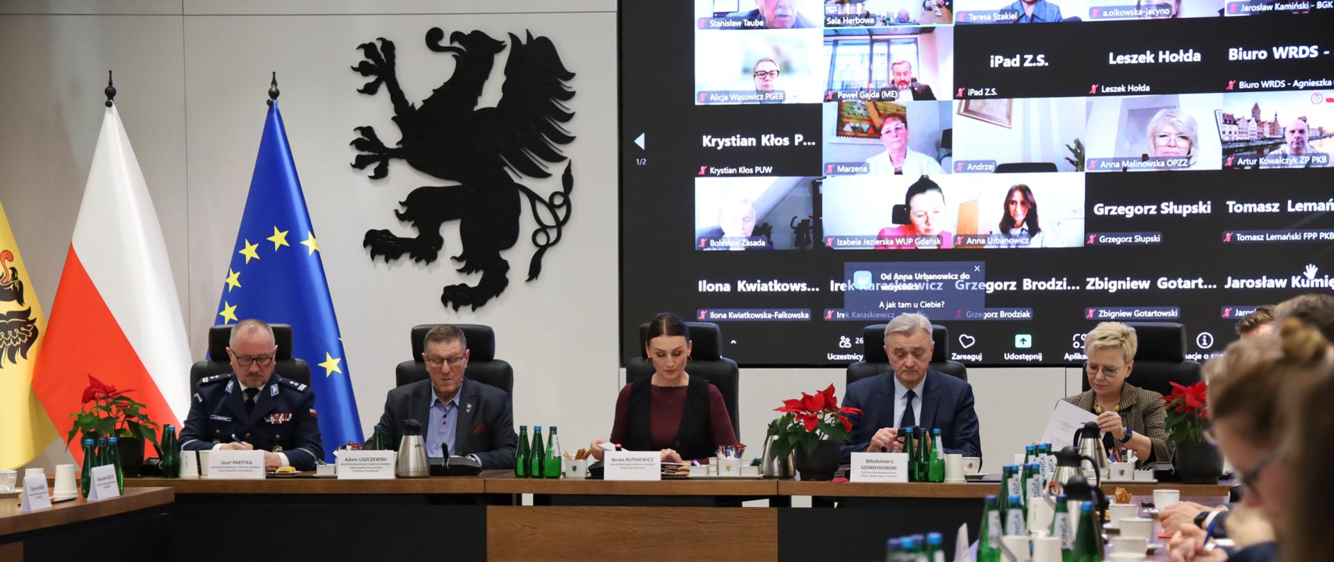 grupa osób siedzi w sali i dyskutuje, w tle gryf -godło województwa