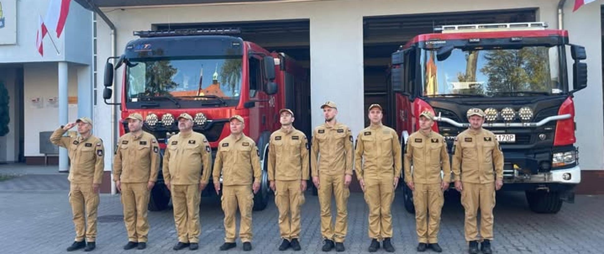Zbiórka strażaków przed jednostką na tle samochodów pożarniczych