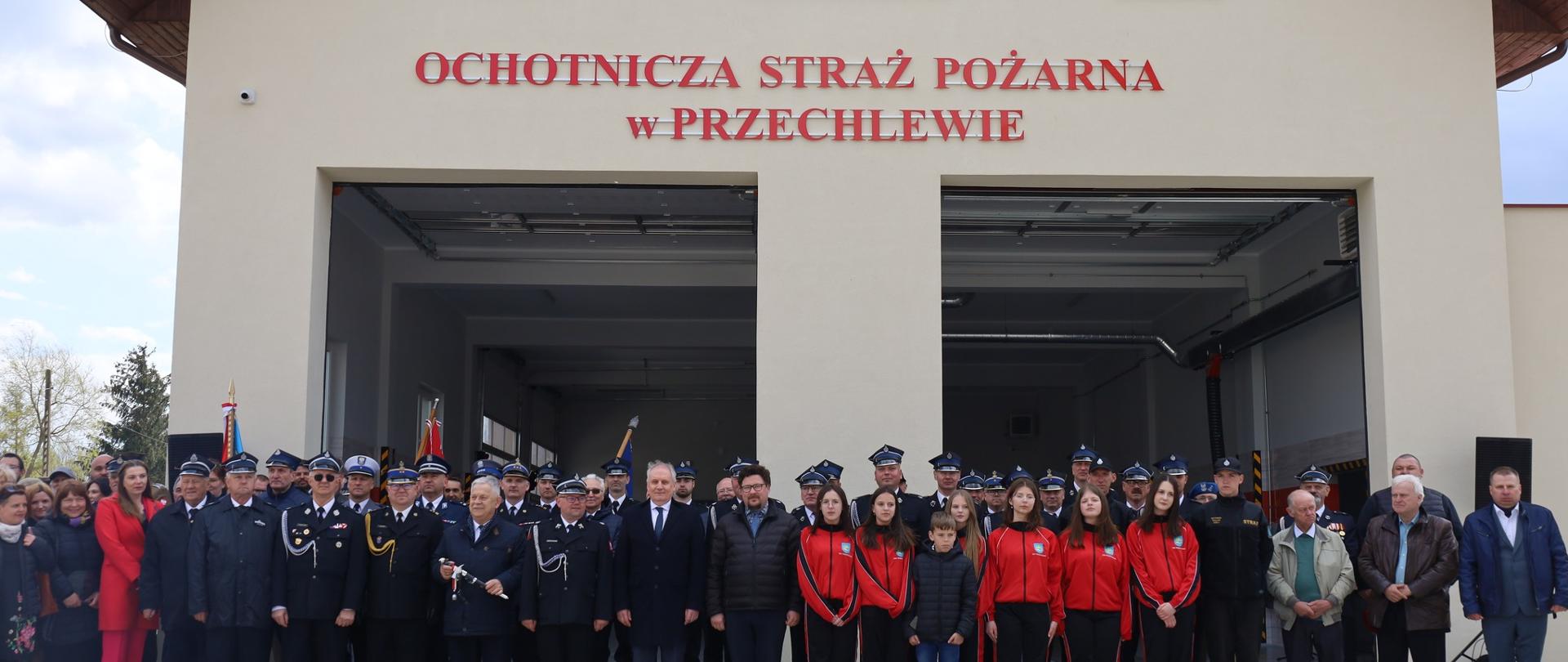 Zdjęcie grupowe uczestników uroczystego apelu z okazji otwarcia nowej remizy Ochotniczej Straży Pożarnej w Przechlewie. Goście i uczestnicy stoją przed budynkiem nowej remizy.