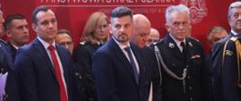 Na zdjęciu od lewej widać Dyrektora Biura Wojewody Jarosława Dragucia oraz Zastępcę Dyrektora Biura Obsługi Urzędu Krzysztofa Klisia. Za nimi widać pozostałych uczestników uroczystości. W tle widać czerwone banery z napisem "Państwowa Straż Pożarna".
