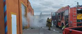 Za zdjęciu widzimy zadymienie wydobywające się z budynku remizy OSP oraz strażaka ubierającego aparat powietrzny, a obok samochód pożarniczy