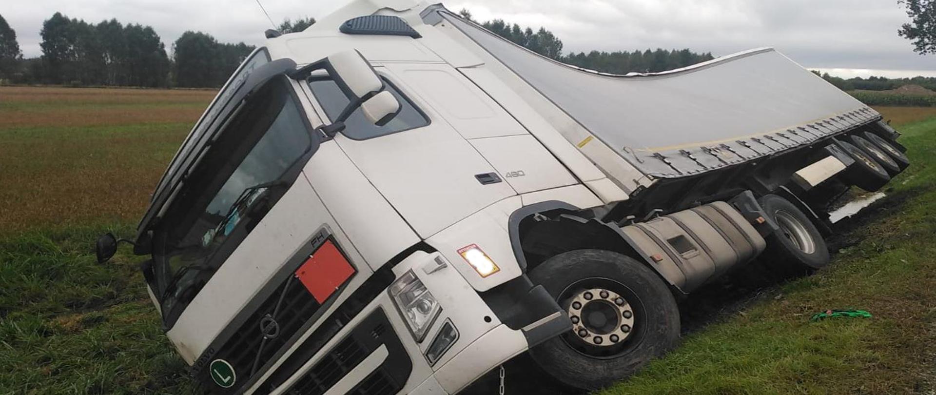 Zdjęcie przedstawia samochód ciężarowy który zjechał do przydrożnego rowu i prawym bokiem opiera się o skarpę rowu.