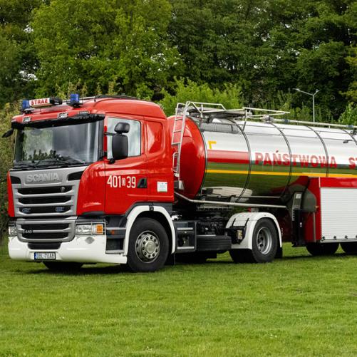 Ciężki ciągnik siodłowy Scania G440 (numer „401[D]39”) z podpiętą dużą, chromowaną naczepą-cysterną. Na błyszczącym boku cysterny widnieje czerwony napis „PAŃSTWOWA STRAŻ POŻARNA”. Cały zestaw stoi na zielonym terenie.