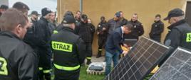 strażacy państwowej i ochotniczej straży pożarnej stoją przy panelach fotowoltaicznych podczas Szkolenia z zasad postępowania podczas zdarzeń z samochodami osobowymi z napędem elektrycznym oraz w obrębie instalacji fotowoltaicznych