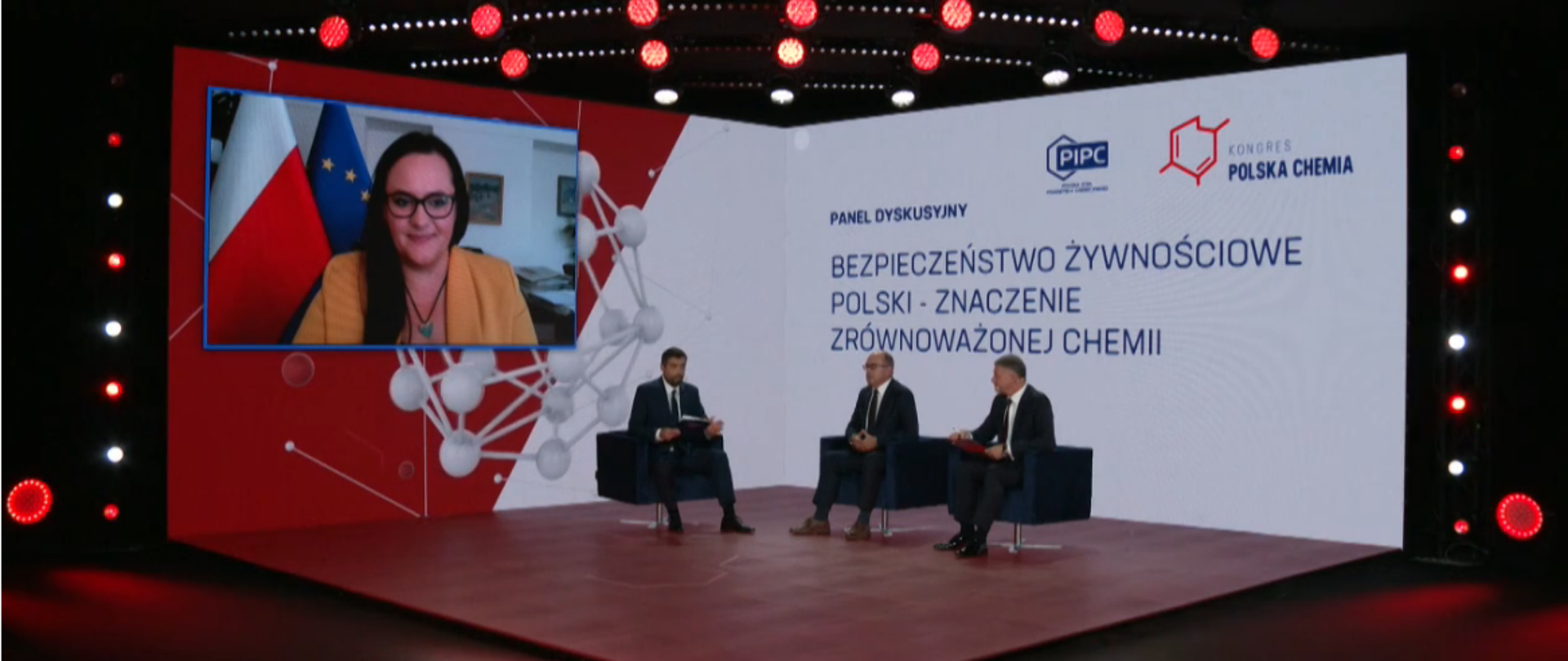 Na scenie w fotelach siedzi trzech mężczyzn. Na ekranie wiszącym na ścianie widać minister Jarosińską-Jedynak.