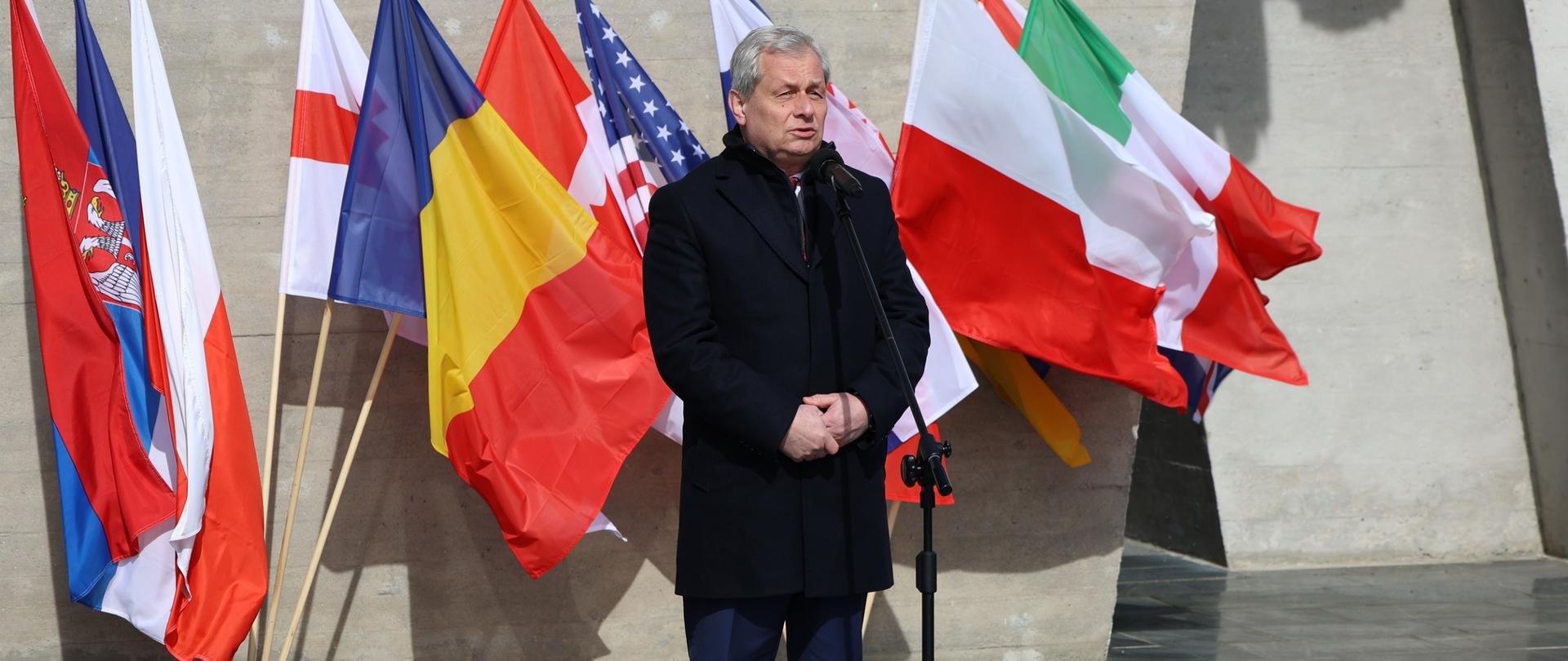 Wojewoda Opolski stoi przed mikrofonem, w tle flagi narodowe. 