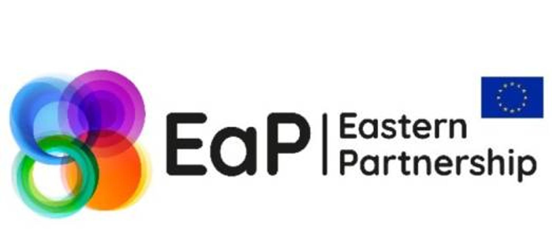 logotyp Partnerstwa Wschodniego: pośrodku skrót EaP, i angielska nazwa Eastern Partnership, po lewej cztery tęczowe, połączone ze sobą koła, a po prawej - flaga UE