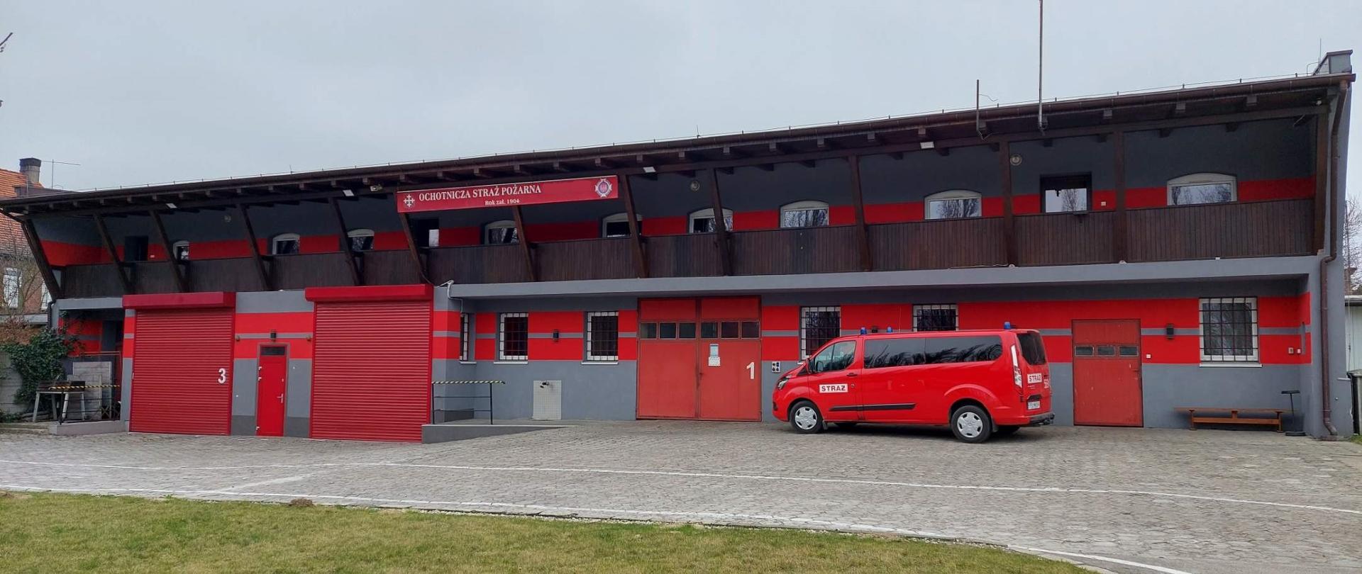 widok na front remizy OSP przed którą stoi czerwony bus osobowy