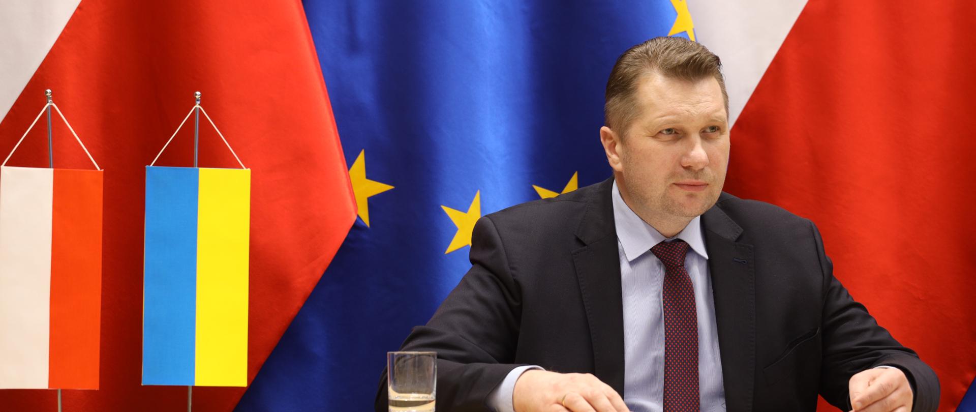 Minister siedzi przy stole z flagami Polski i Ukrainy.