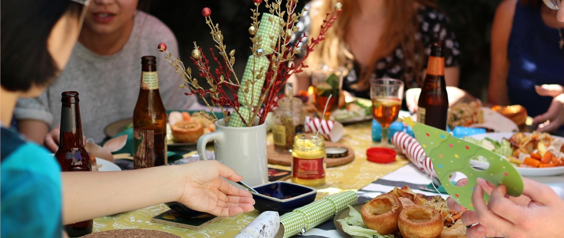 Kilka osób siedzi przy zastawionym stole i prowadzi rozmowę. 