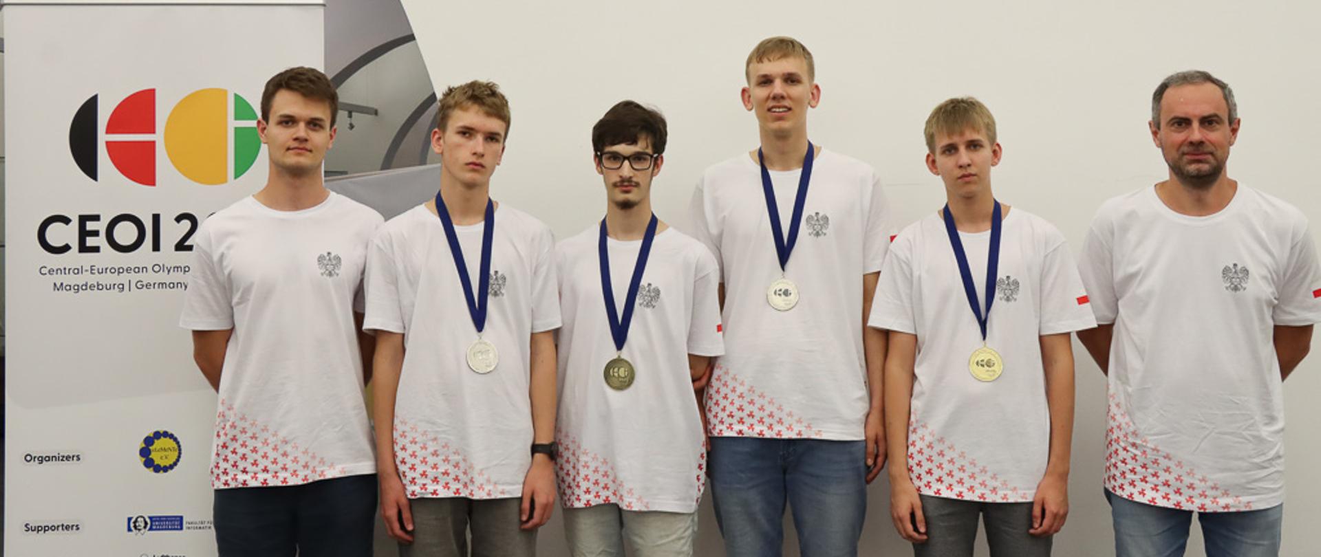 Pięciu młodych mężczyzn z opiekunem pozuje do zdjęcia. Na szyi czterech z nich zawieszone są na niebieskich szarfach medale.