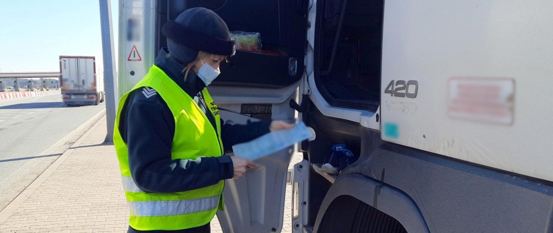 Inspektor wielkopolskiej ITD stoi obok ciężarówki i kontroluje dokumenty okazane przez kierowcę.