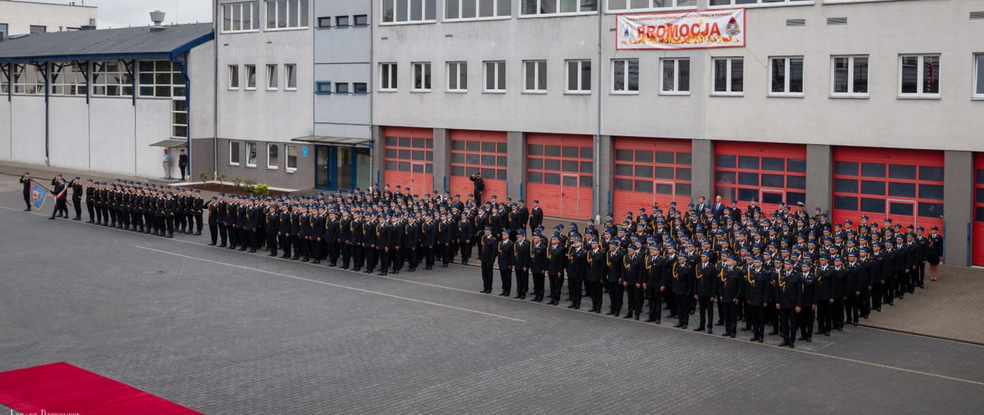 Zdjęcie przedstawia strażaków podczas nominację na stopień młodszego aspiranta, strażacy stoją w szykzu na placu.
