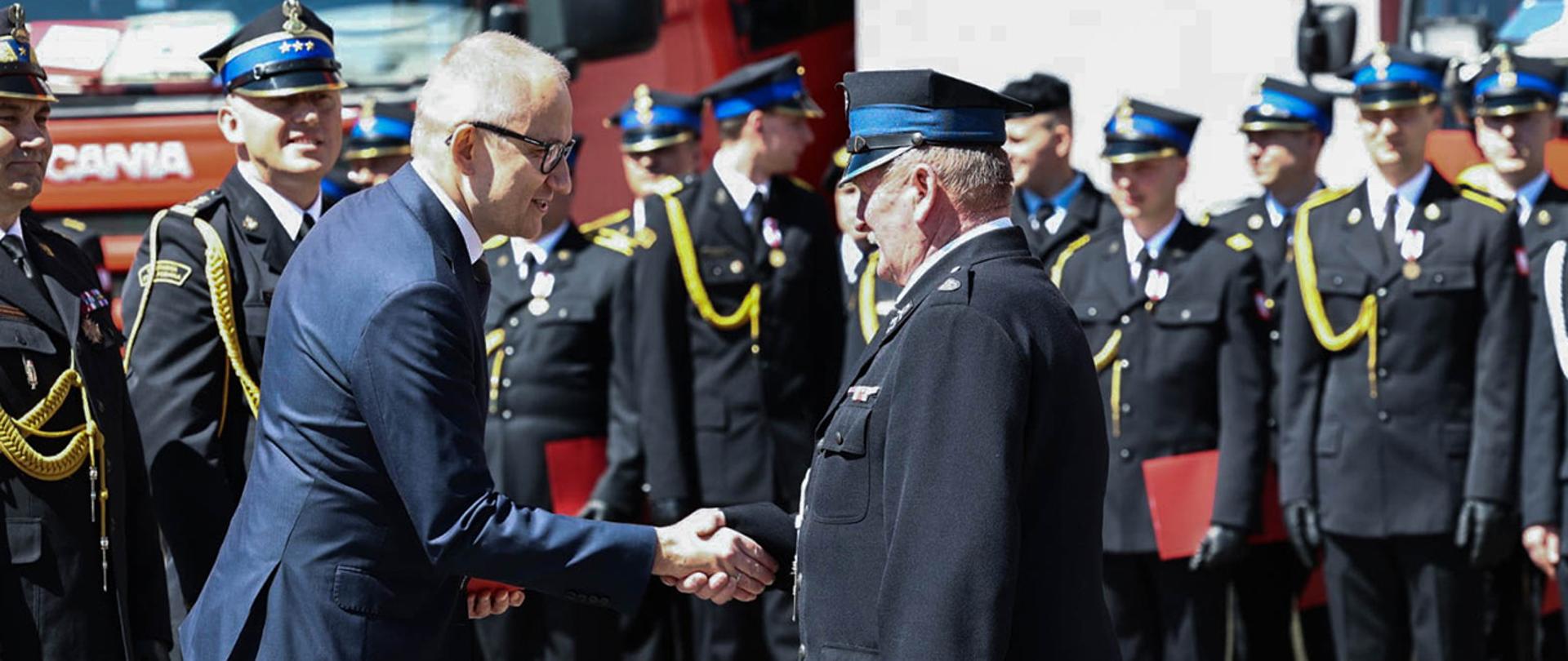 Wiceminister Błażej Poboży wręczający strażakowi-ochotnikowi decyzję w sprawie przyznania świadczeń ratowniczych.