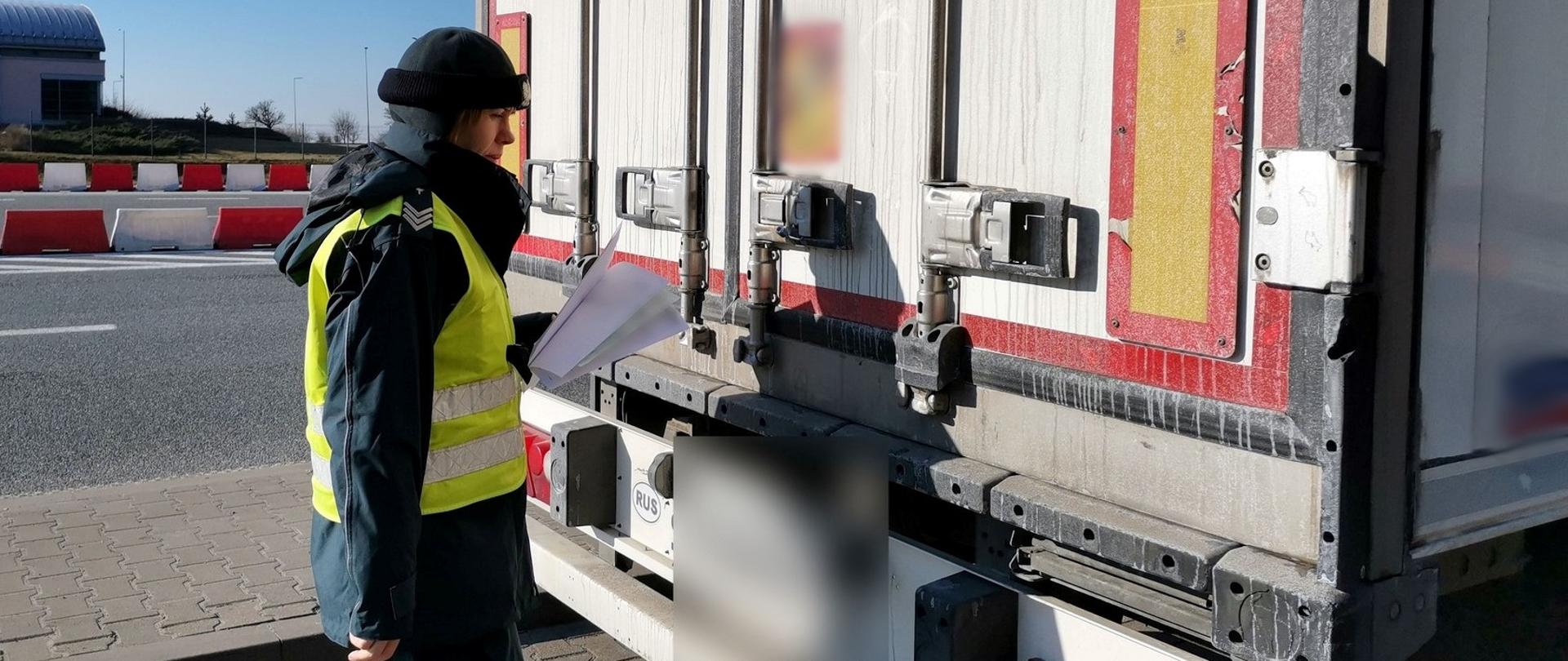 Inspektor wielkopolskiej ITD trzyma w ręku dokumenty pobrane do kontroli i stoi z tyłu naczepy ciężarowej.