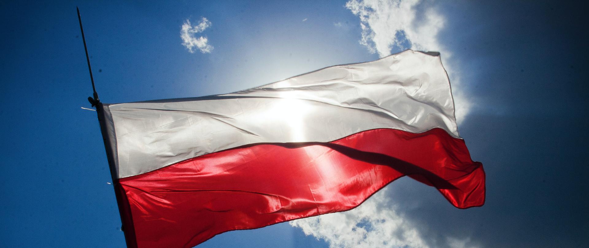 Biało Czerwona Flaga powiewa na tle błękitnego nieba zasłaniając słońce
