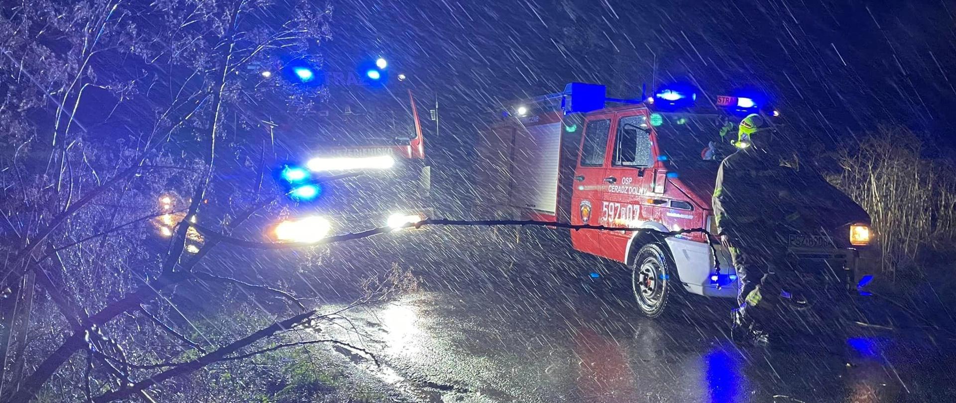 Dwa samochody strażackie na drodze, jest noc, pada deszcz