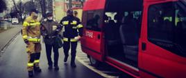 Strażacy prowadzą osobę do samochodu strażackiego
