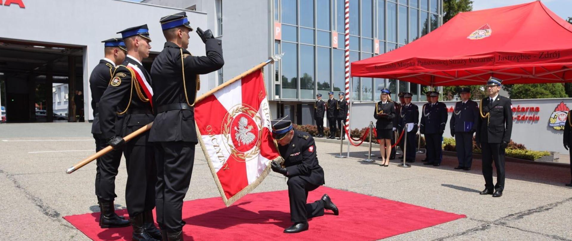 bryg. Jan Cepiel Komendant Miejski PSP w Jastrzębiu-Zdroju oddaje honor sztandarowi Komendy Miejskiej PSP w Jastrzębiu-Zdroju przed pocztem sztandarowym. W tle trybuna honorowa i budynek komendy
