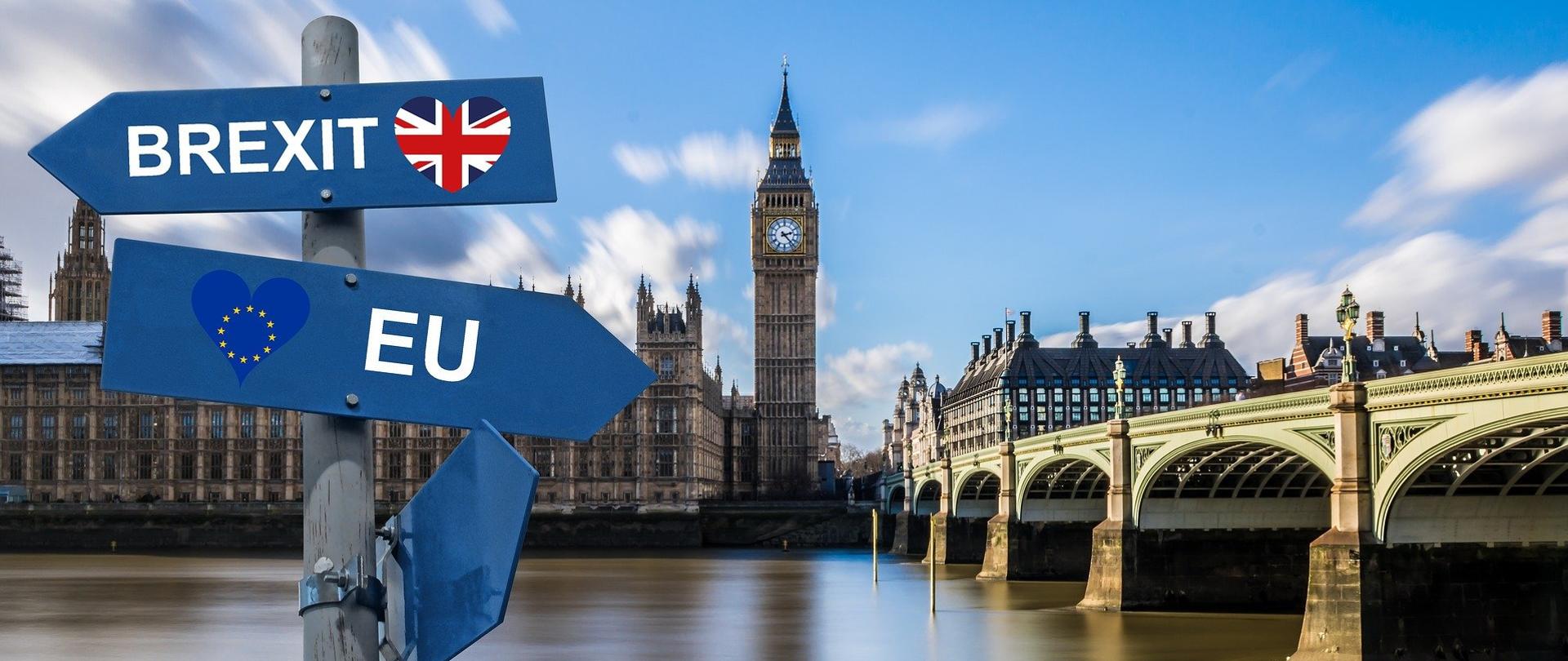Po lewej stronie kadru widnieje drogowskaz z niebieskimi dwoma tablicami. Jedna z nich wskazuje kierunek Brexitu. Druga, skierowana w prawą stronę wskazuje na Europę. W tle Big Ben oraz londyński most. 